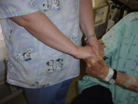 Picture of a female Nurse holding an elderly patient's hand.